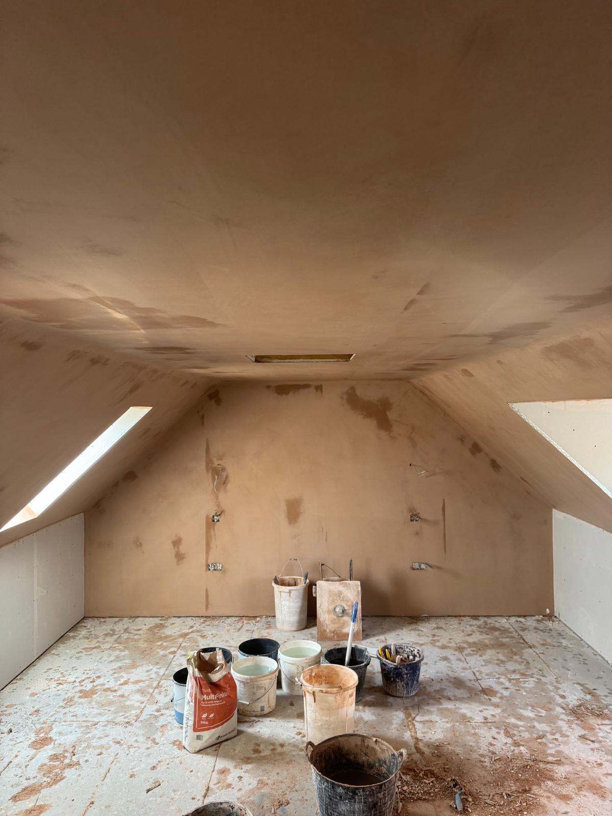 A loft room mid-job, with sloped ceilings plastered and tools on the floor